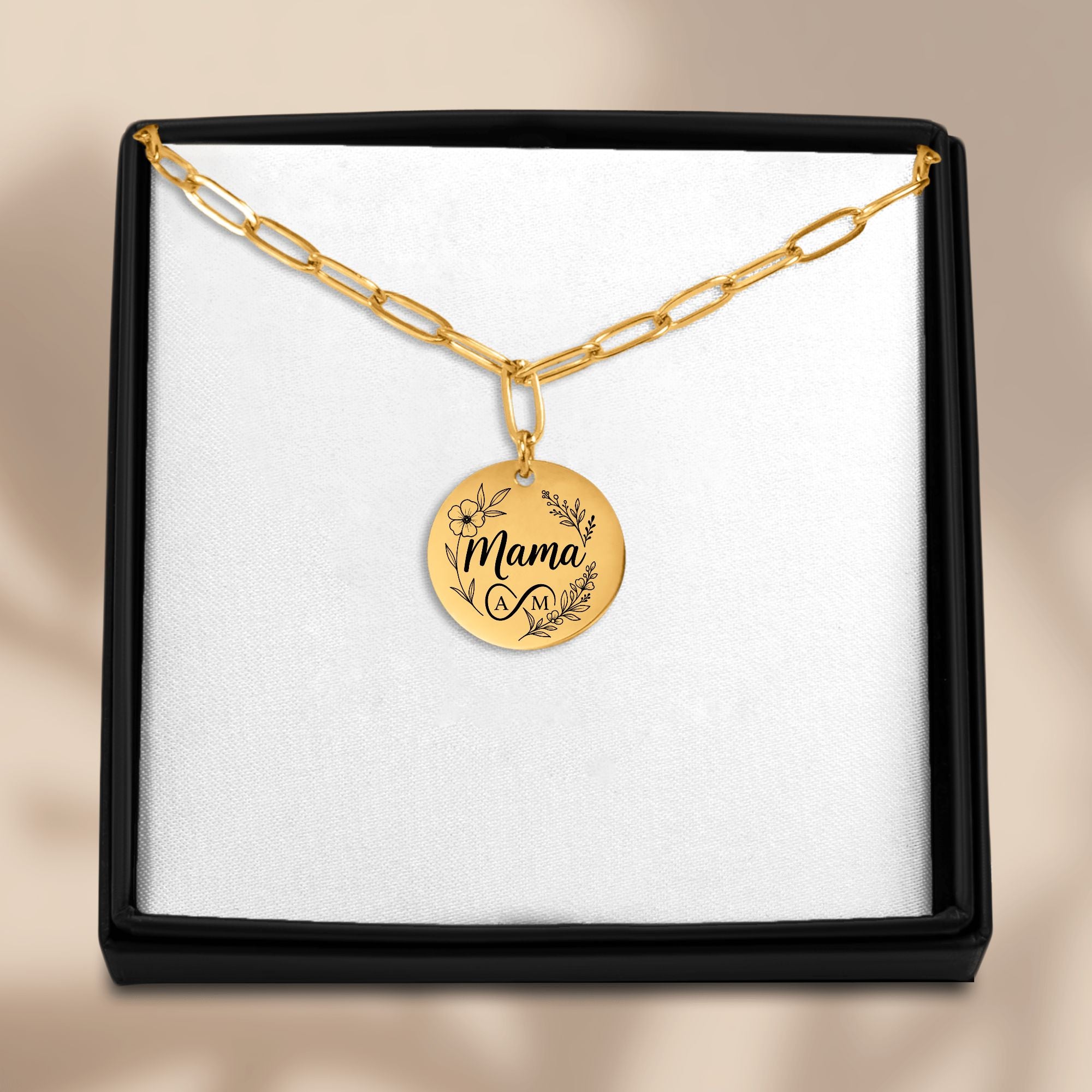 Gold necklace with 'Mama' pendant in a black box on a beige background