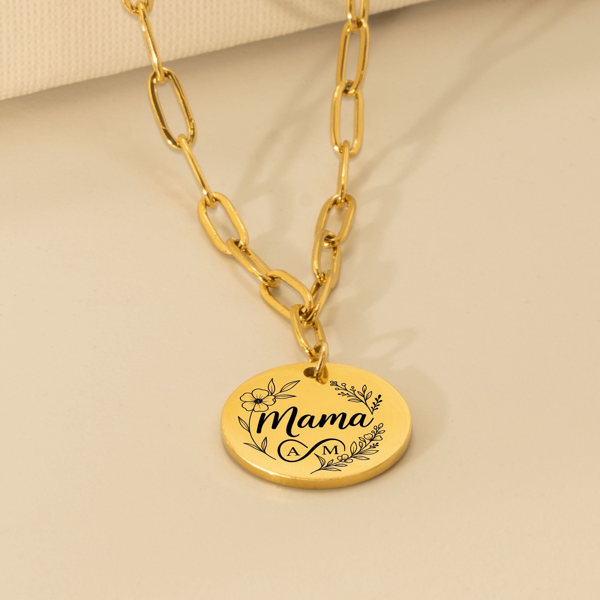 Gold necklace with a round pendant engraved with 'Mama' on a beige background